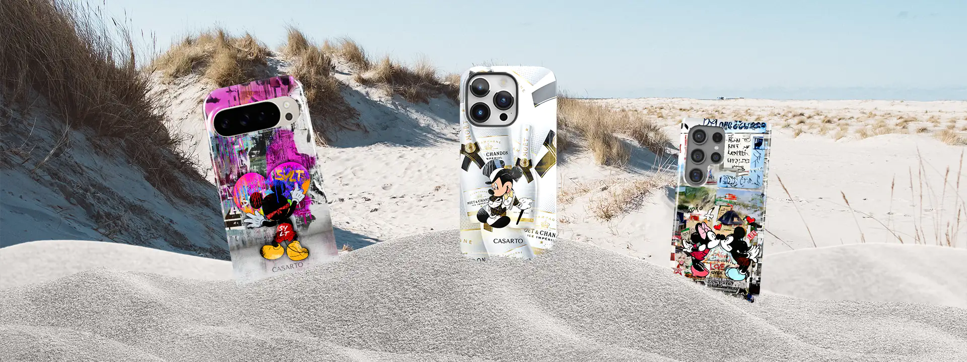 Drei Handyhüllen aus der Sylt Kollektion mit Motiven von Mickey Mouse, Minnie Mouse und Champagnerflaschen vor einem Strand-Hintergrund.