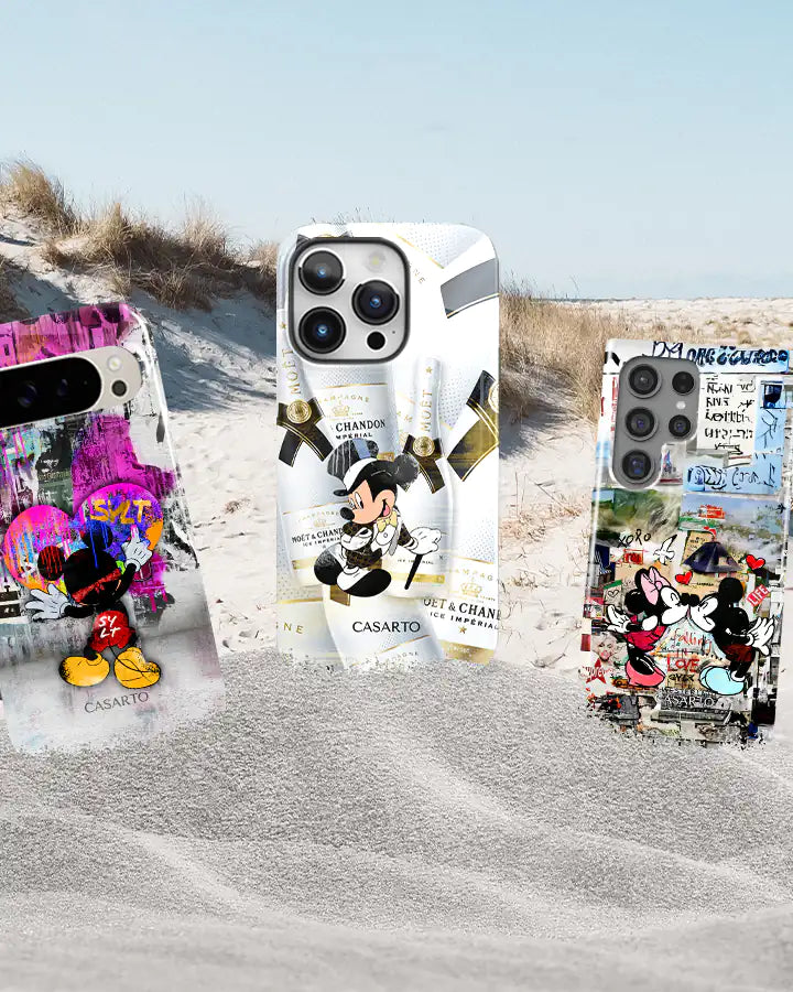 Drei Handyhüllen aus der Sylt Kollektion mit Motiven von Mickey Mouse, Minnie Mouse und Champagnerflaschen vor einem Strand-Hintergrund.